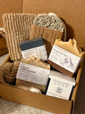 Box of natural skincare and body care products including soap bars and cream.